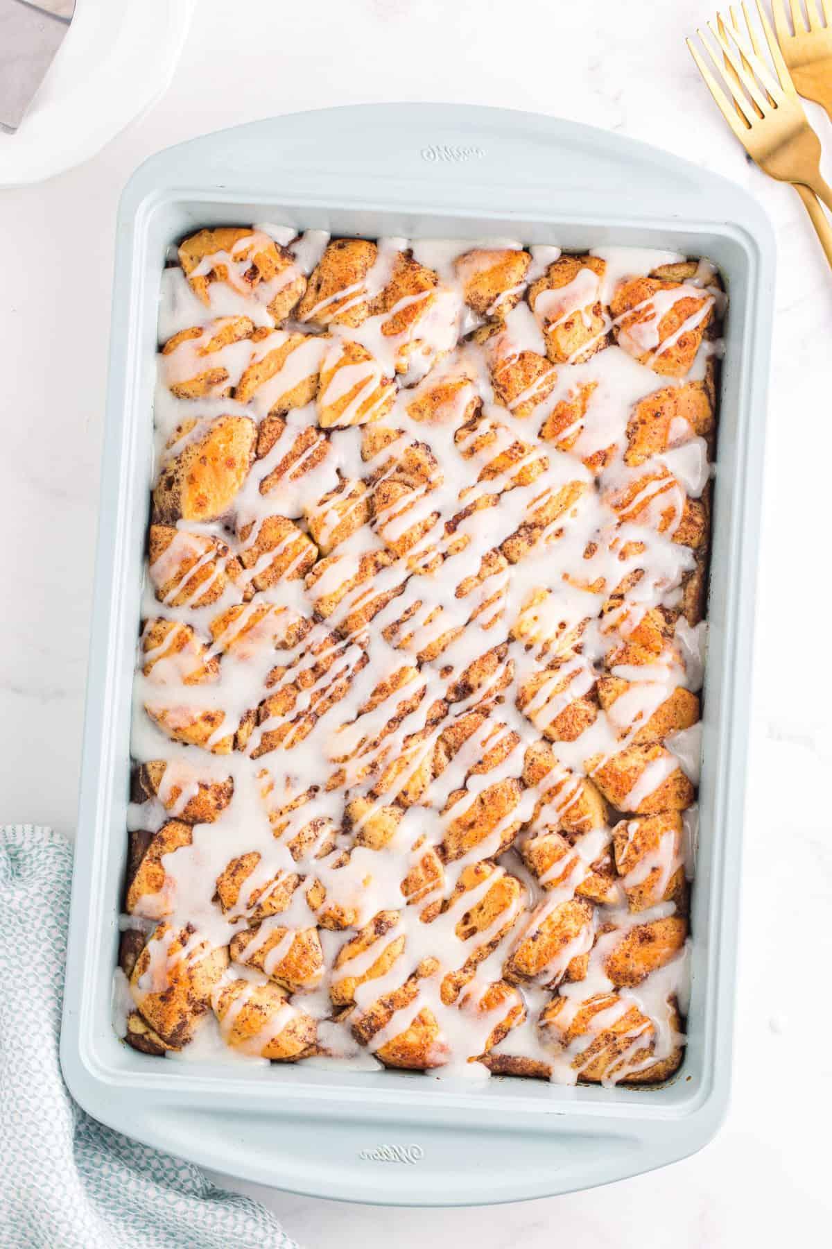 cinnamon roll casserole with icing drizzled on top in light blue baking dish