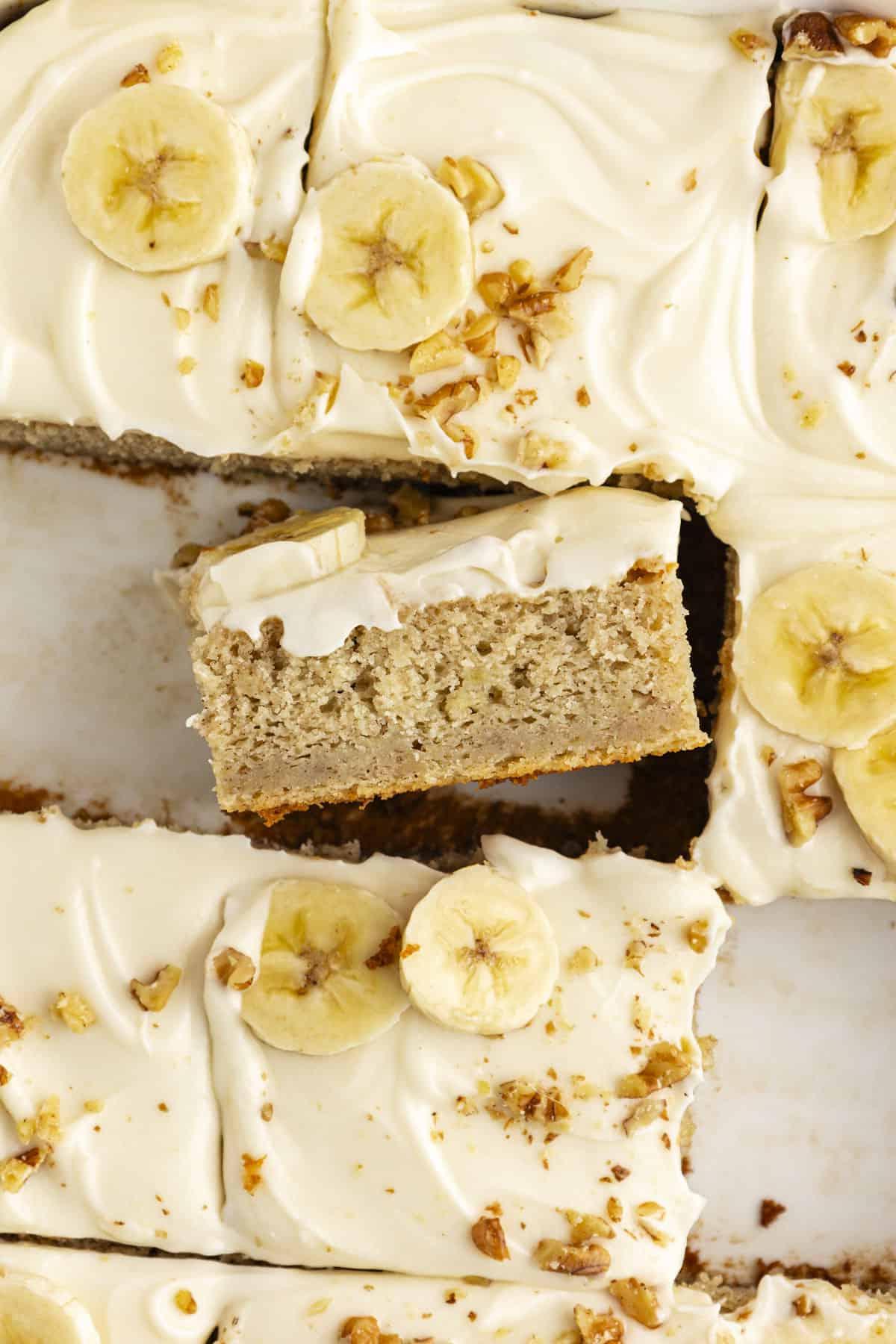 Una fetta ravvicinata di torta di banane con alcune fette mancanti e una fetta girata su un lato in modo da poter vedere lo strato di torta e lo strato di glassa sopra