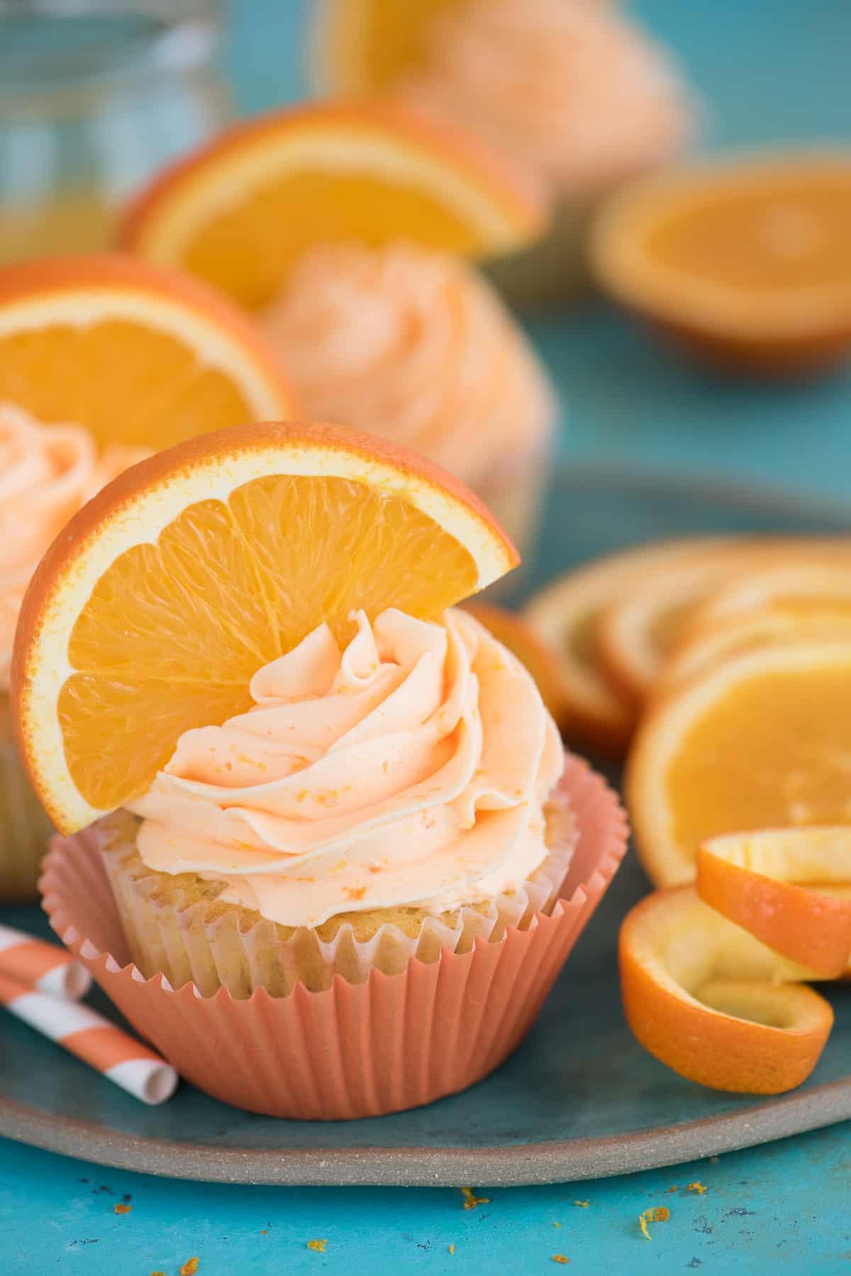 I Cupcake all'Arancia e Semi di Papavero sono una ricetta unica di cupcake agrumati, realizzati con vero succo e scorza d'arancia! Cupcake all'Arancia e Semi di Papavero con fetta d'arancia su sfondo blu