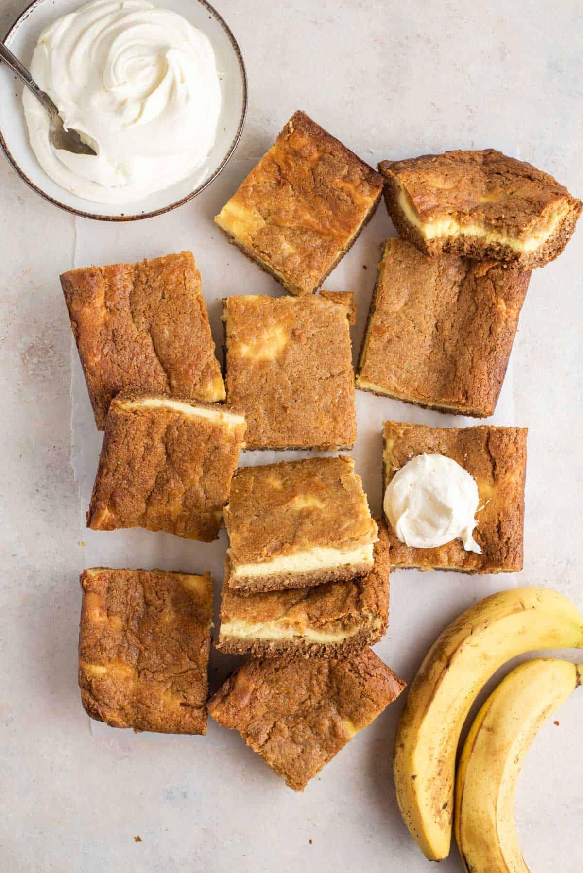 Brownies al budino di banana disposti su un bancone con banane e una ciotola di panna montata