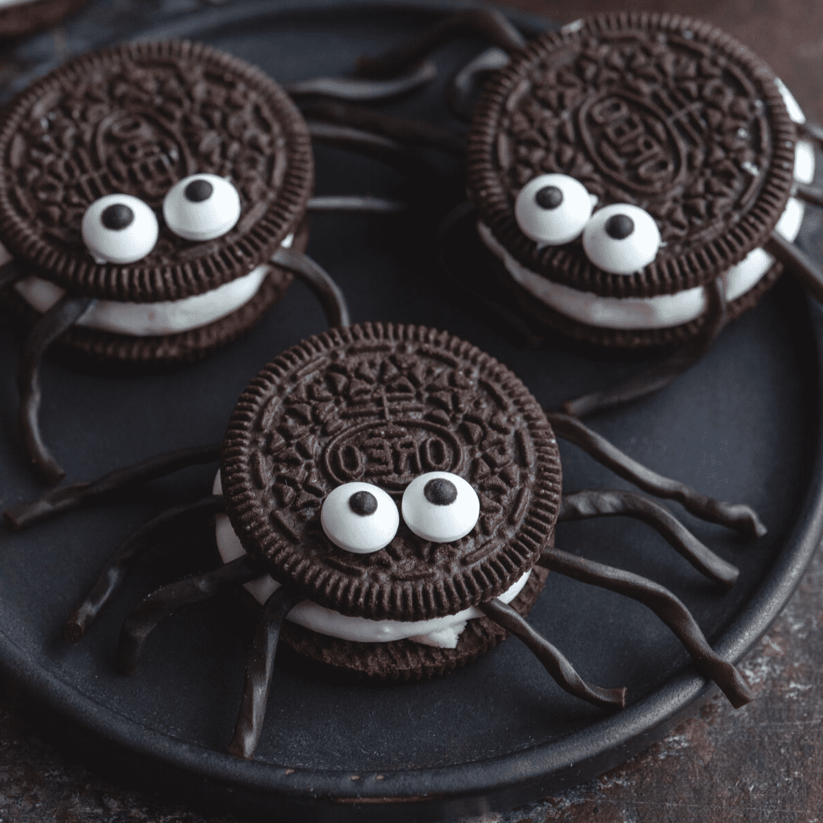Tre ragni di Oreo rifiniti e pronti, poggiati su un piatto nero scuro, perfetti per Halloween