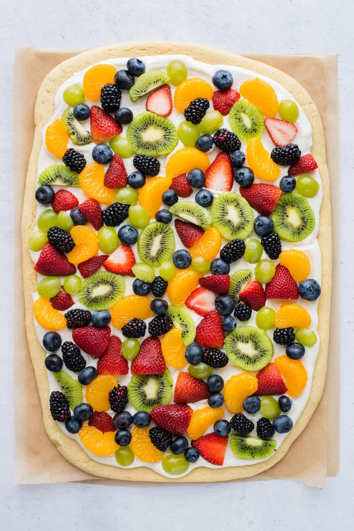 La Migliore Ricetta di Pizza alla Frutta 2 Una pizza di frutta intera con fragole, mirtilli, mandarini, kiwi e uva su carta da forno marrone