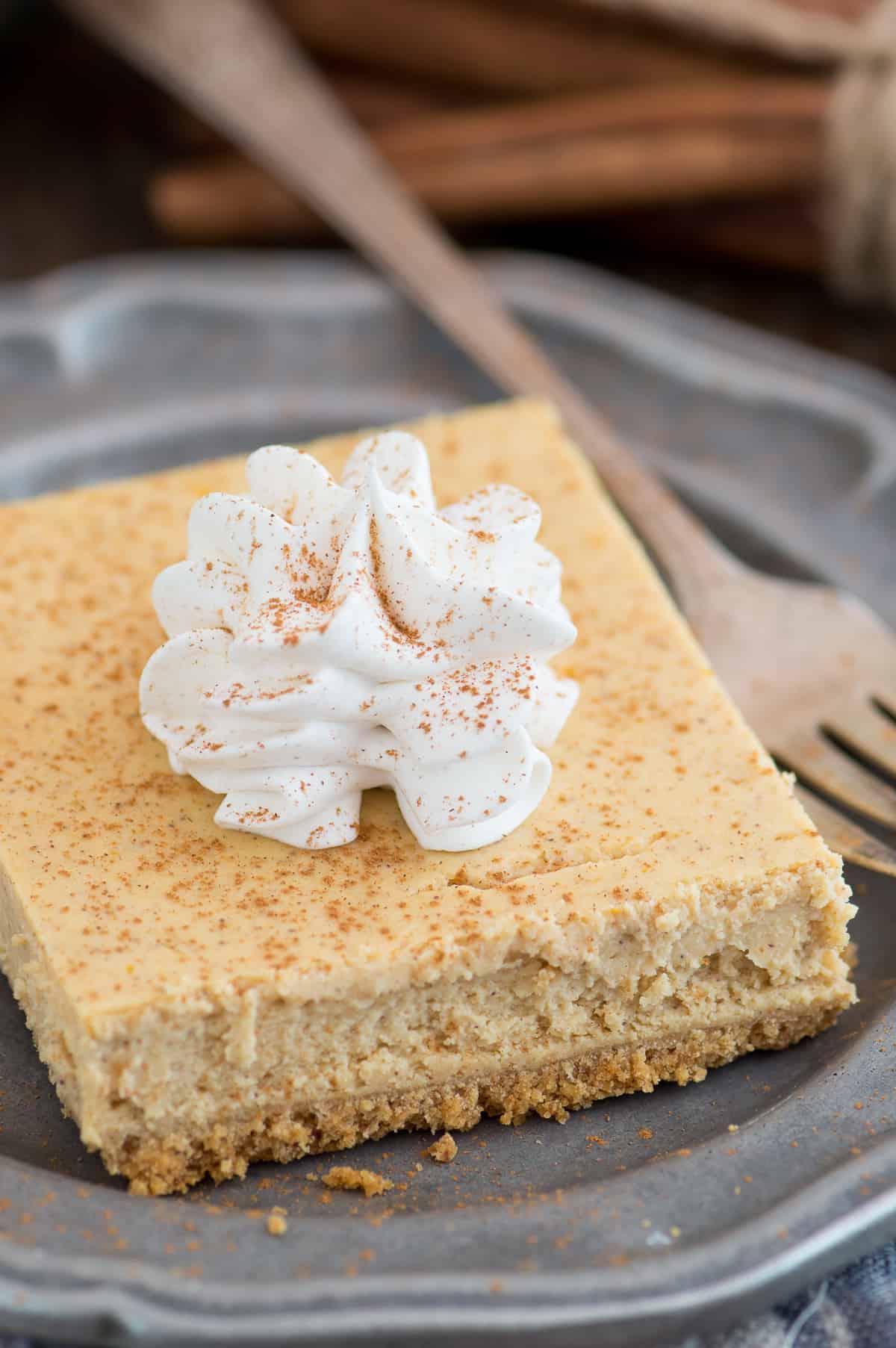 Fetta di barretta di cheesecake alla zucca con una cucchiaiata di panna montata su un piatto di metallo