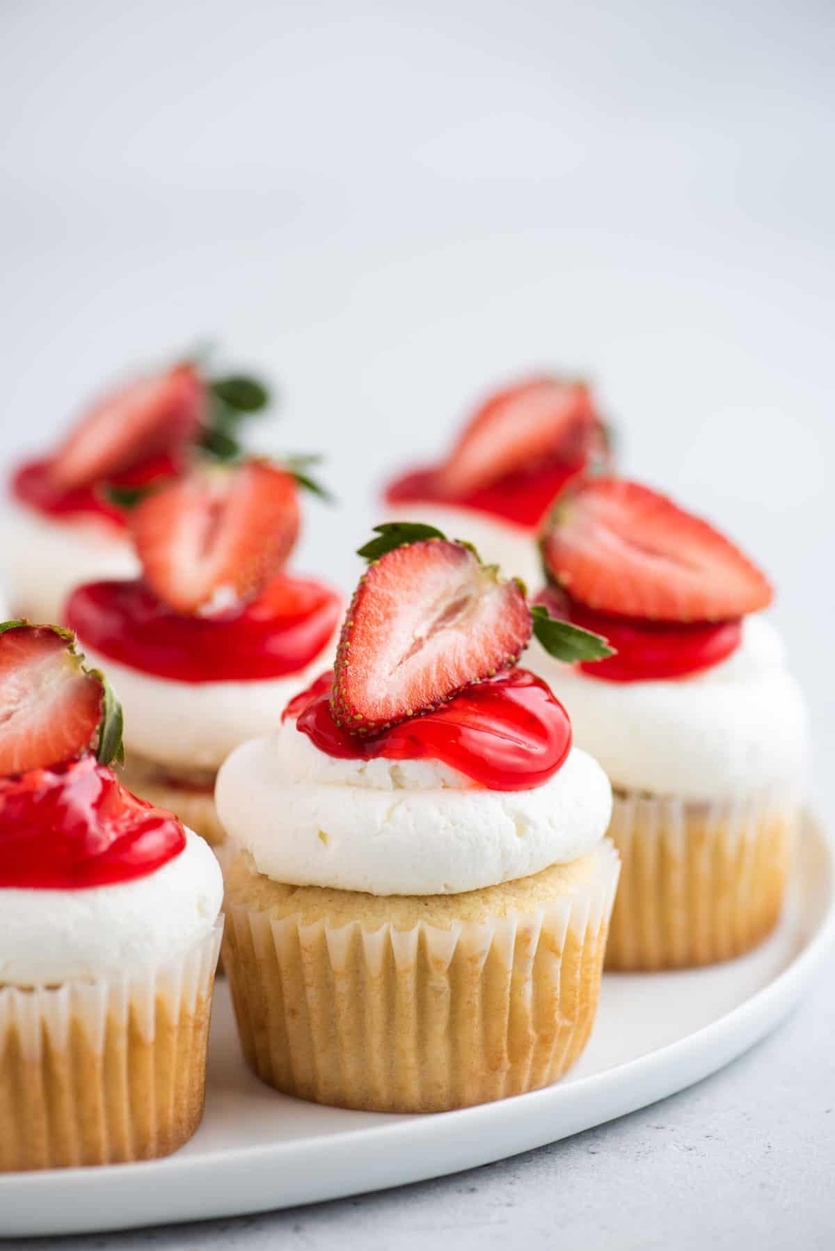 I Cupcake alle Fragole Shortcake sono fatti con torta alla vaniglia umida, ripieni di dolce salsa di fragole e ricoperti di soffice panna montata! Cupcake alle fragole shortcake su piatto rotondo