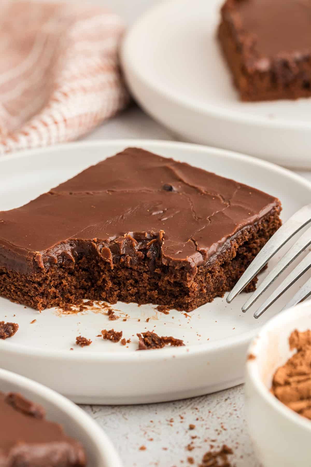 Una fetta di torta Texana al cioccolato su un piatto bianco con una forchetta, con alcuni morsi mancanti e altre fette su piatti intorno