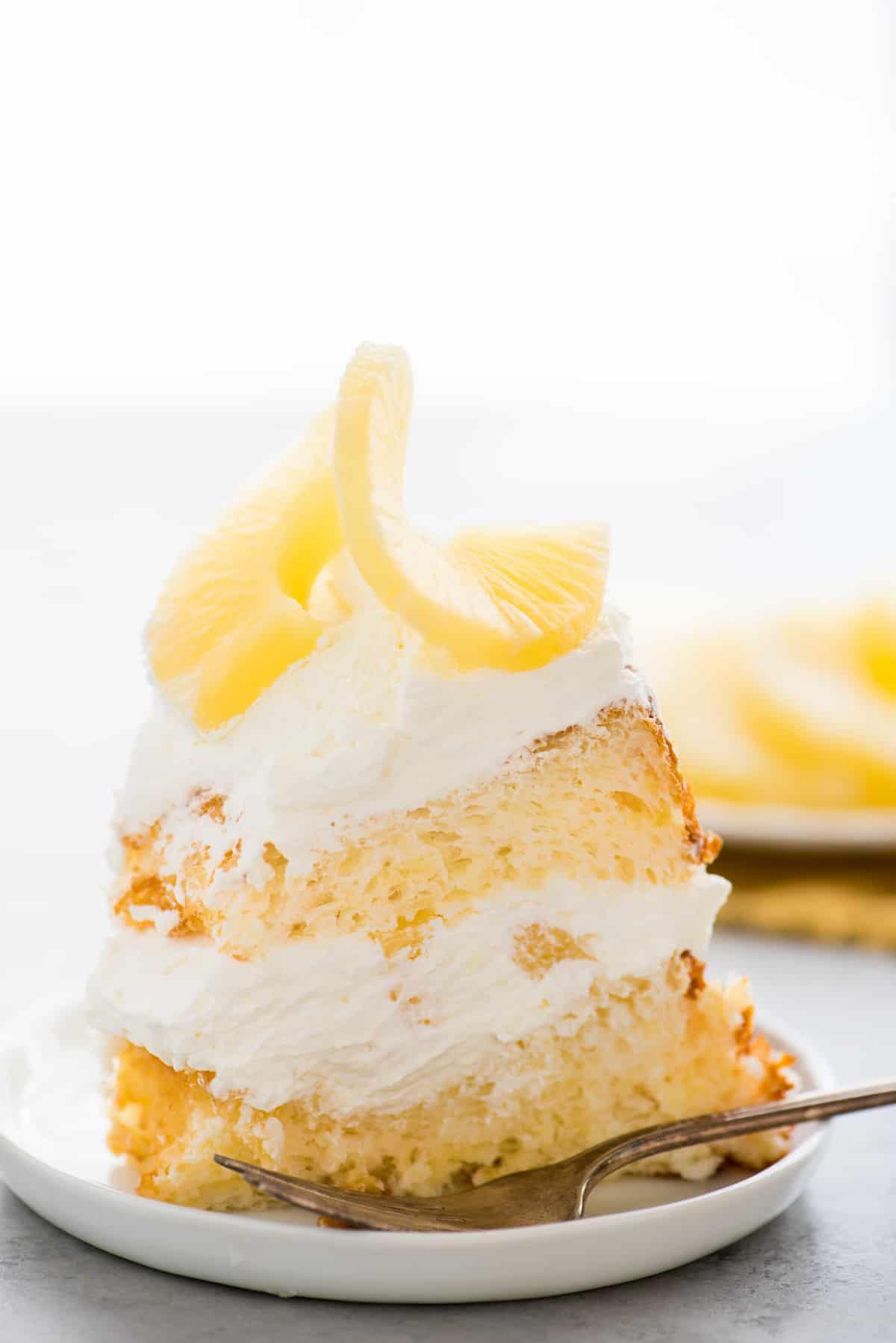 Torta degli angeli all'ananas 2 Fetta di torta Angel Food all'ananas con panna montata e ananas su piatto bianco su sfondo bianco
