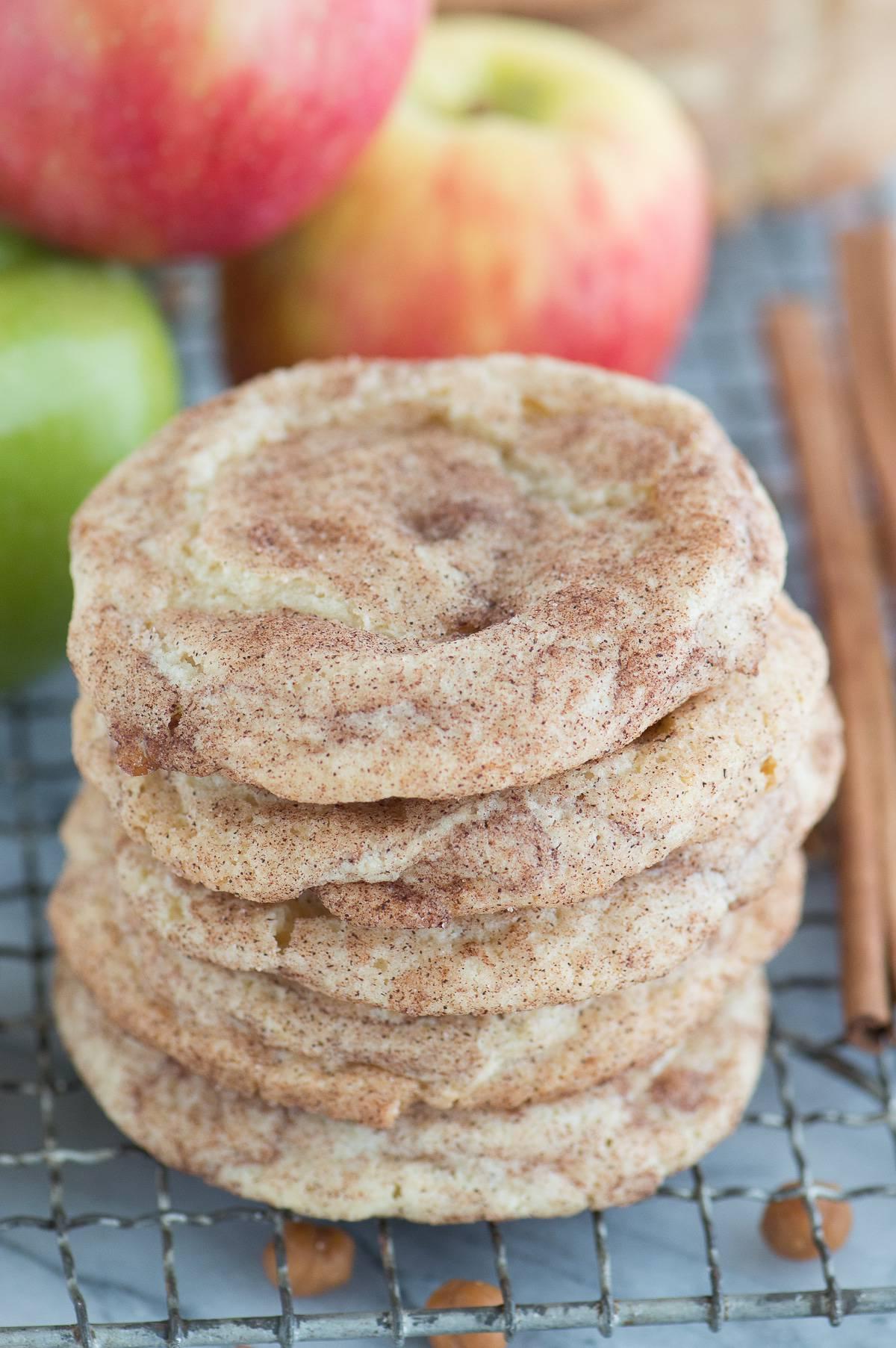Biscotti snickerdoodle alle mele caramellate impilati su una griglia di raffreddamento metallica con mele sullo sfondo