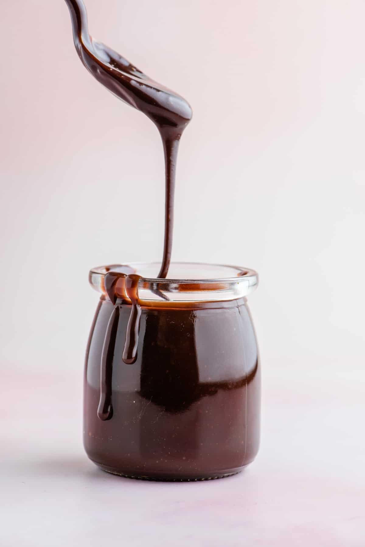 Salsa al cioccolato calda in un barattolo di vetro con un cucchiaio che mostra la salsa densa e calda che gocciola nel barattolo