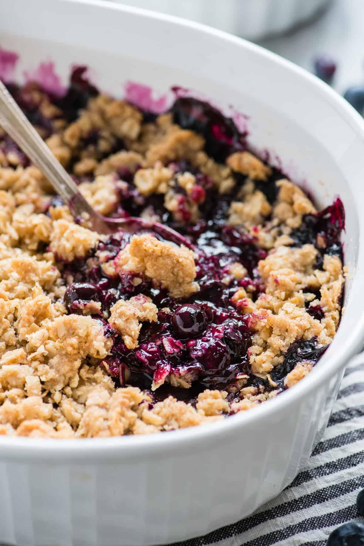 Crumble ai mirtilli in una teglia bianca con un cucchiaio di metallo