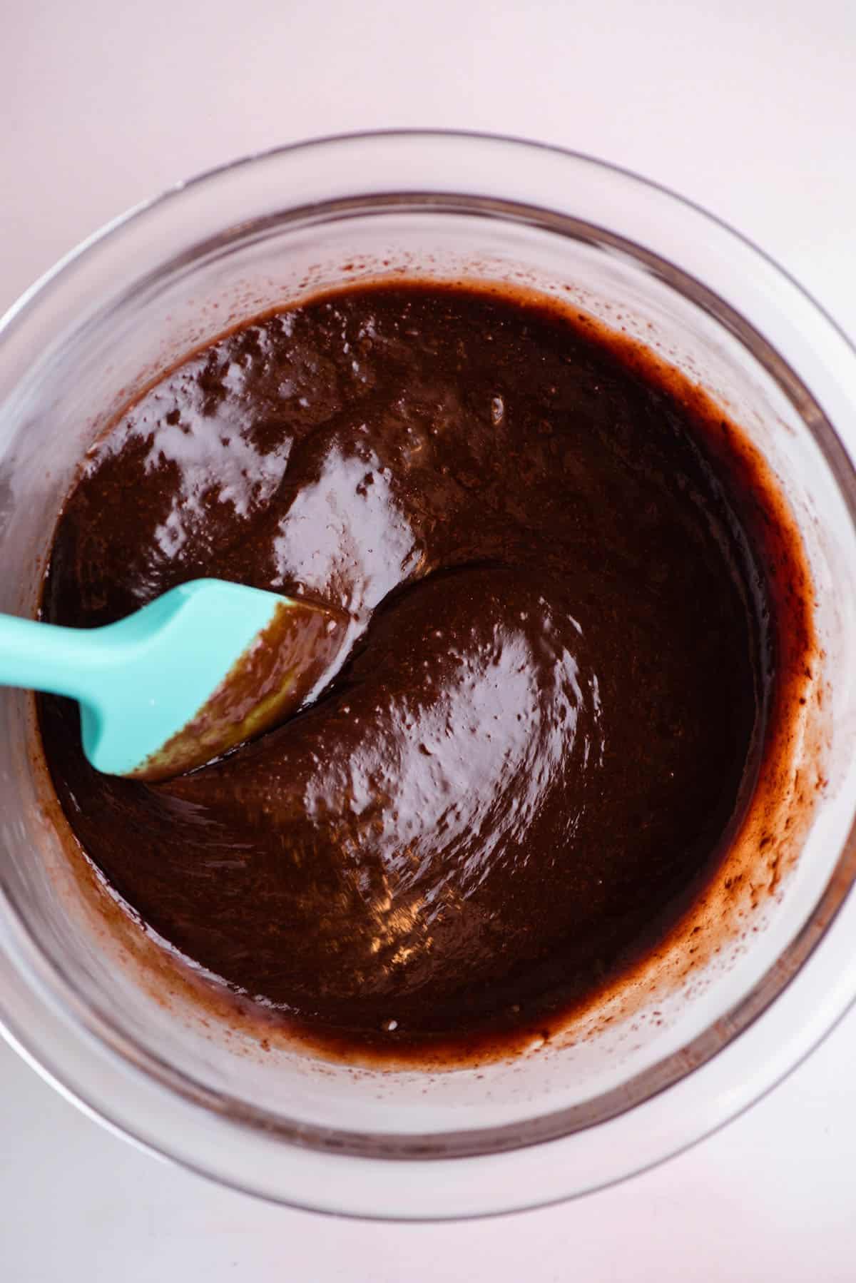Salsa hot fudge in una ciotola di vetro che è stata mescolata con una spatola color verde acqua appoggiata nella ciotola