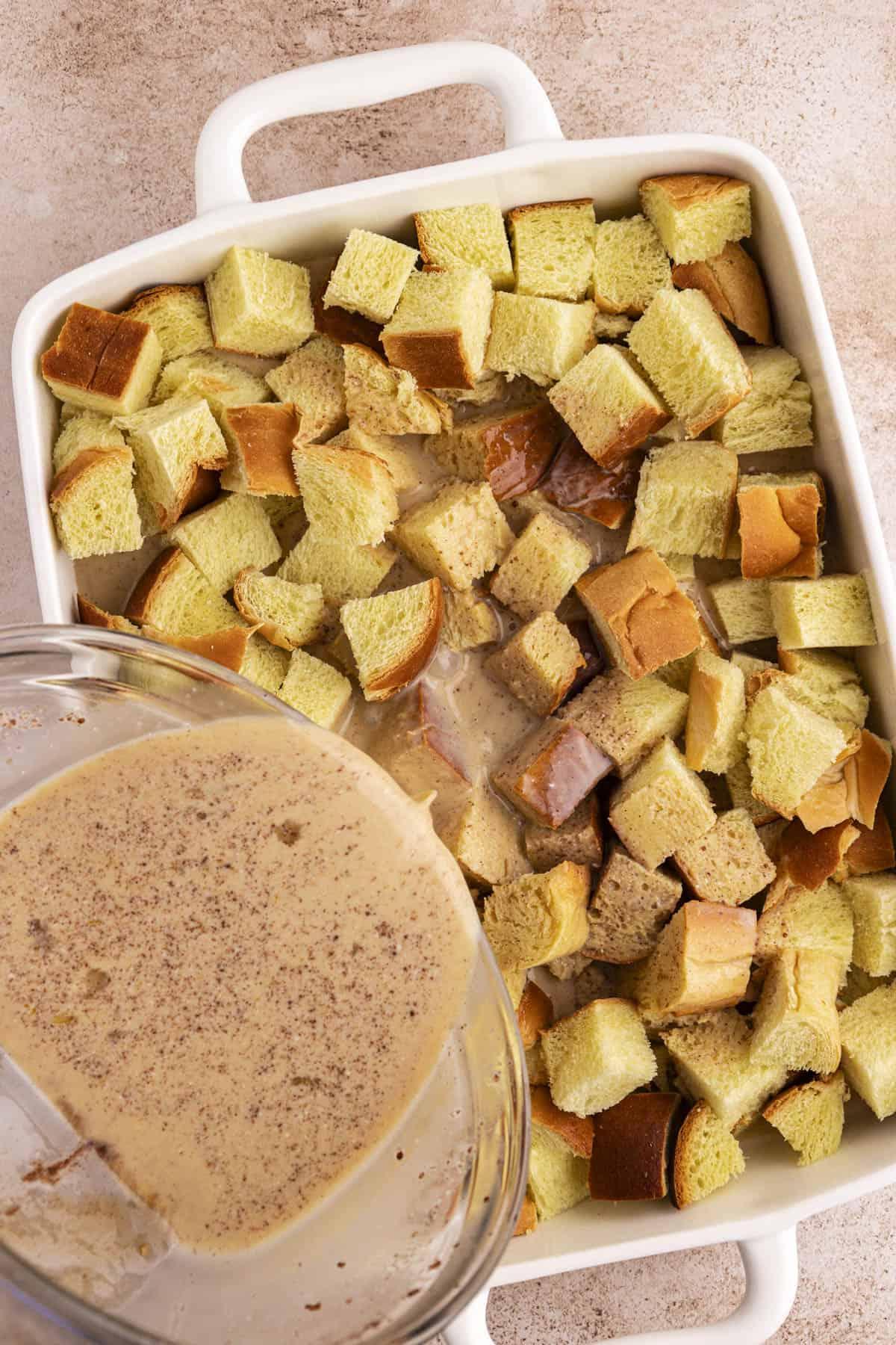 Una teglia bianca piena di cubetti di pane con una miscela liquida versata sopra.