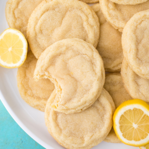 Un piatto di biscotti al limone morbidi e ricoperti di zucchero, con un biscotto al limone morsicato. Fette di limone fresco sono posizionate accanto ai deliziosi biscotti al limone sul piatto.