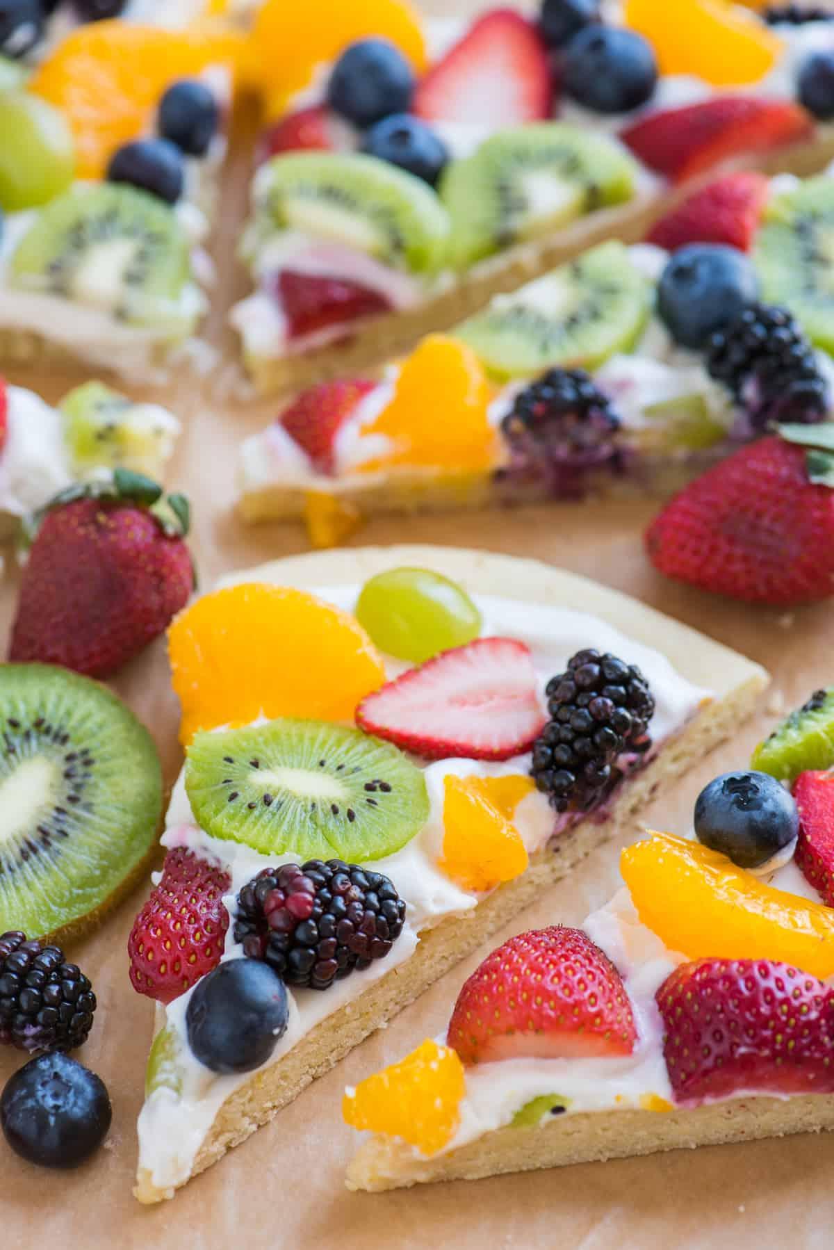 La Migliore Ricetta di Pizza alla Frutta 12 Fetta di pizza di frutta con fragole, mirtilli, mandarini, kiwi e uva su carta da forno marrone