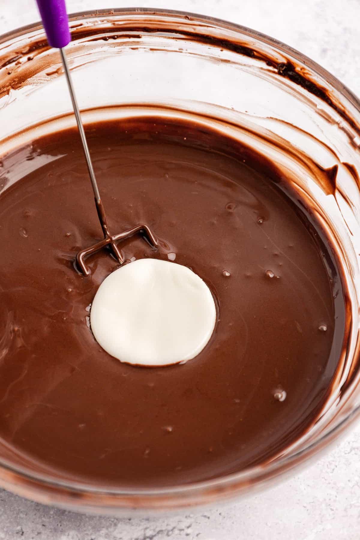 Un disco bianco di ripieno di patty alla menta immerso in una ciotola di vetro trasparente piena di cioccolato fuso