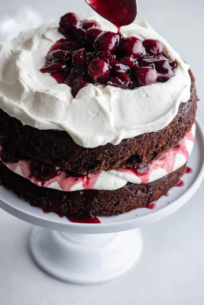 Torta Foresta Nera su un'alzatina bianca con uno strato di torta al cioccolato, panna montata, ciliegie, più torta al cioccolato, più panna montata e ciliegie aggiunte sopra