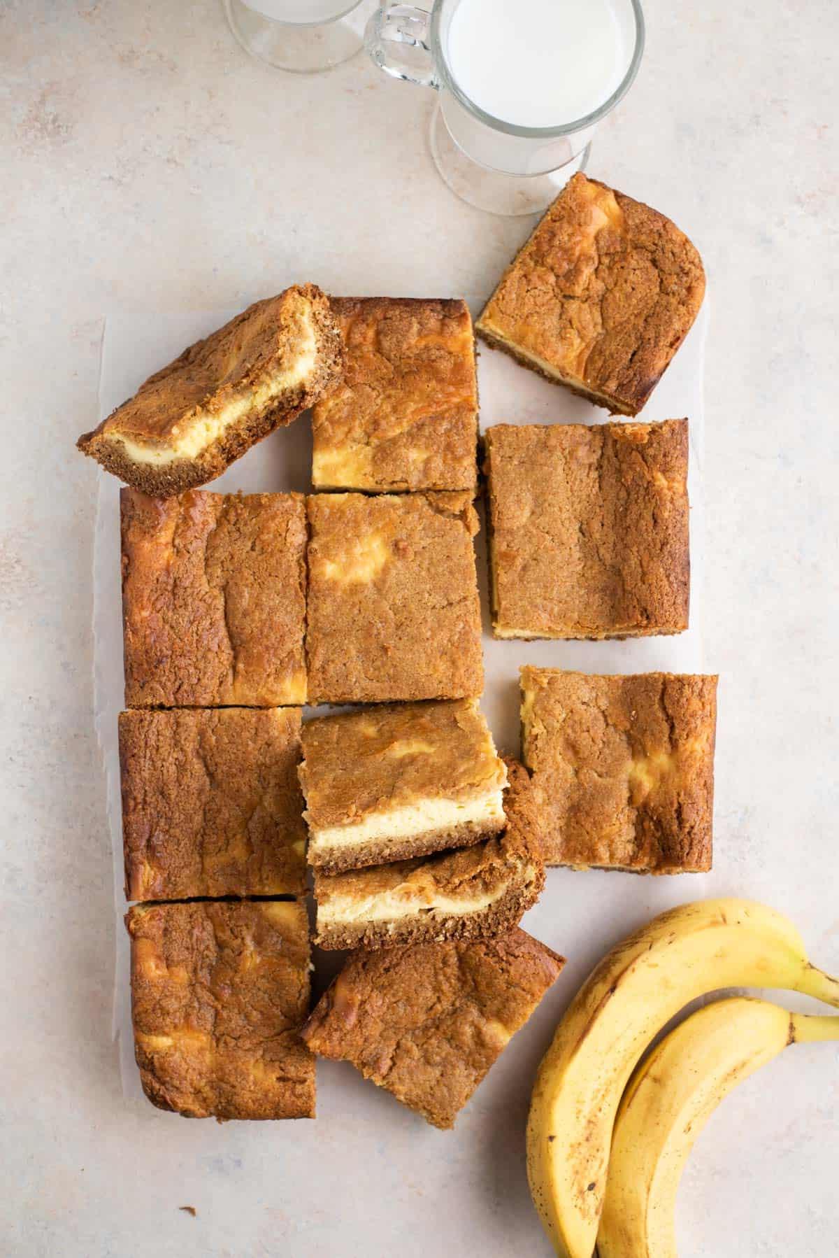 Brownies al budino di banana disposti su un bancone con banane e una tazza di latte