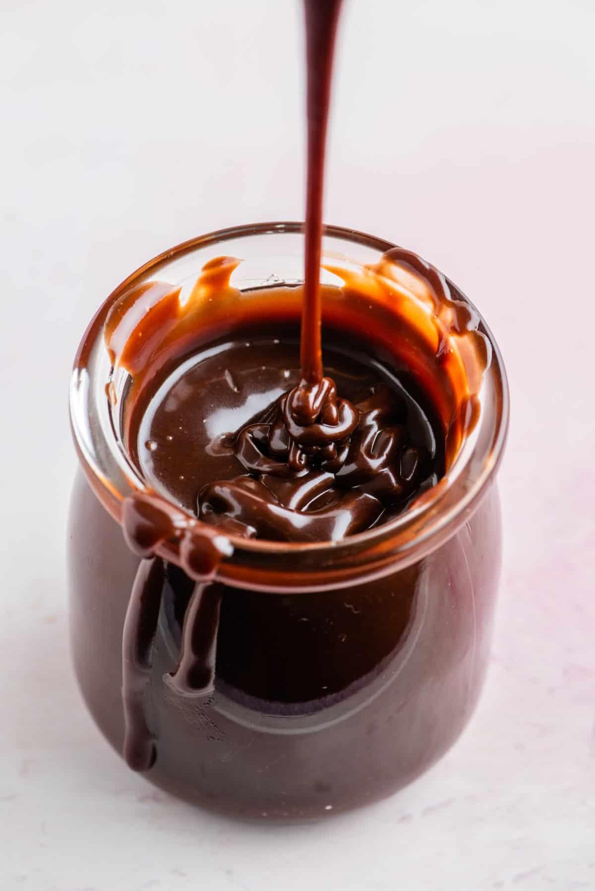 Un barattolo di salsa hot fudge con un filo di salsa che gocciola e salsa che gocciola lungo il lato del barattolo