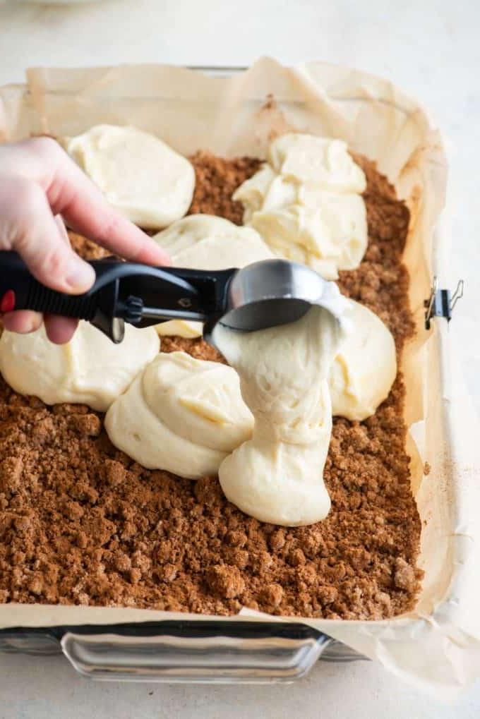 Impasto di torta al caffè versato in una teglia con carta forno con una paletta da gelato sopra il topping di crumble