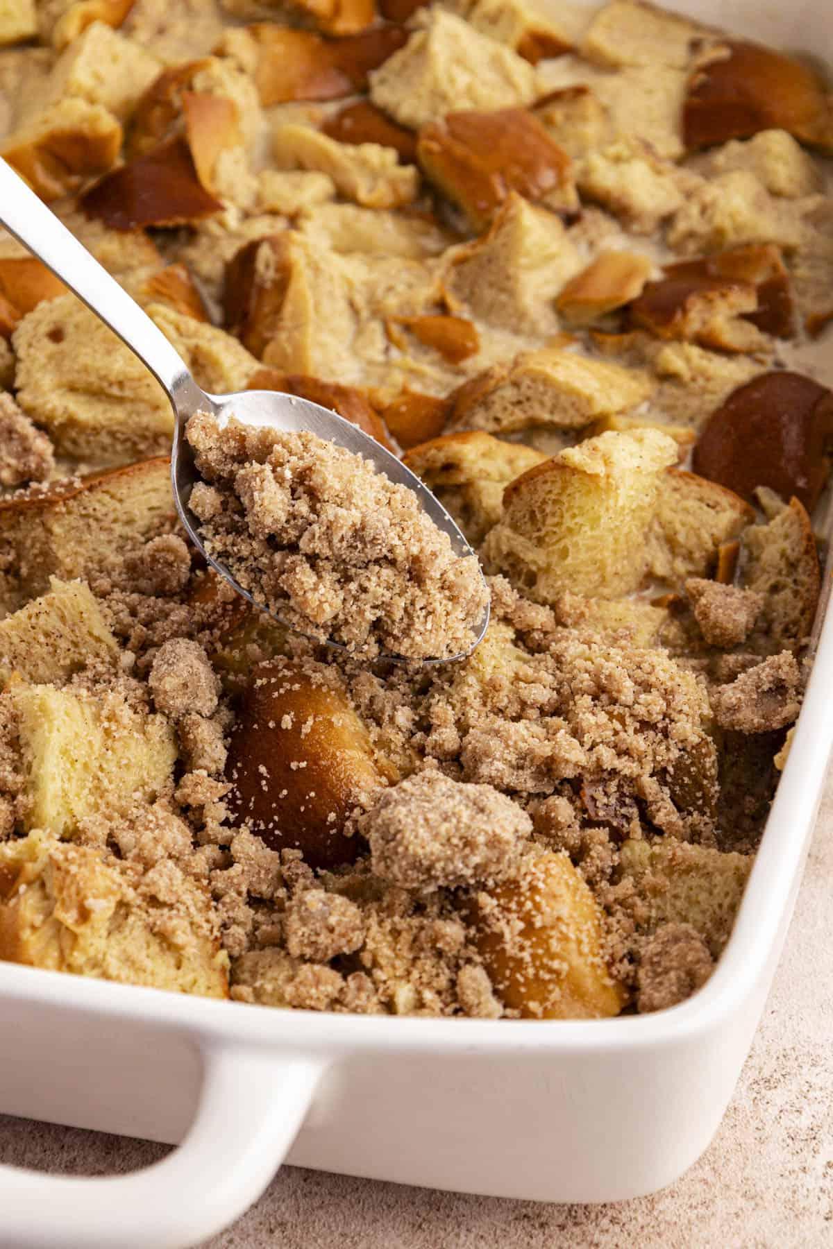 Una teglia bianca con la miscela di French Toast con un cucchiaio di topping croccante spolverato sopra.