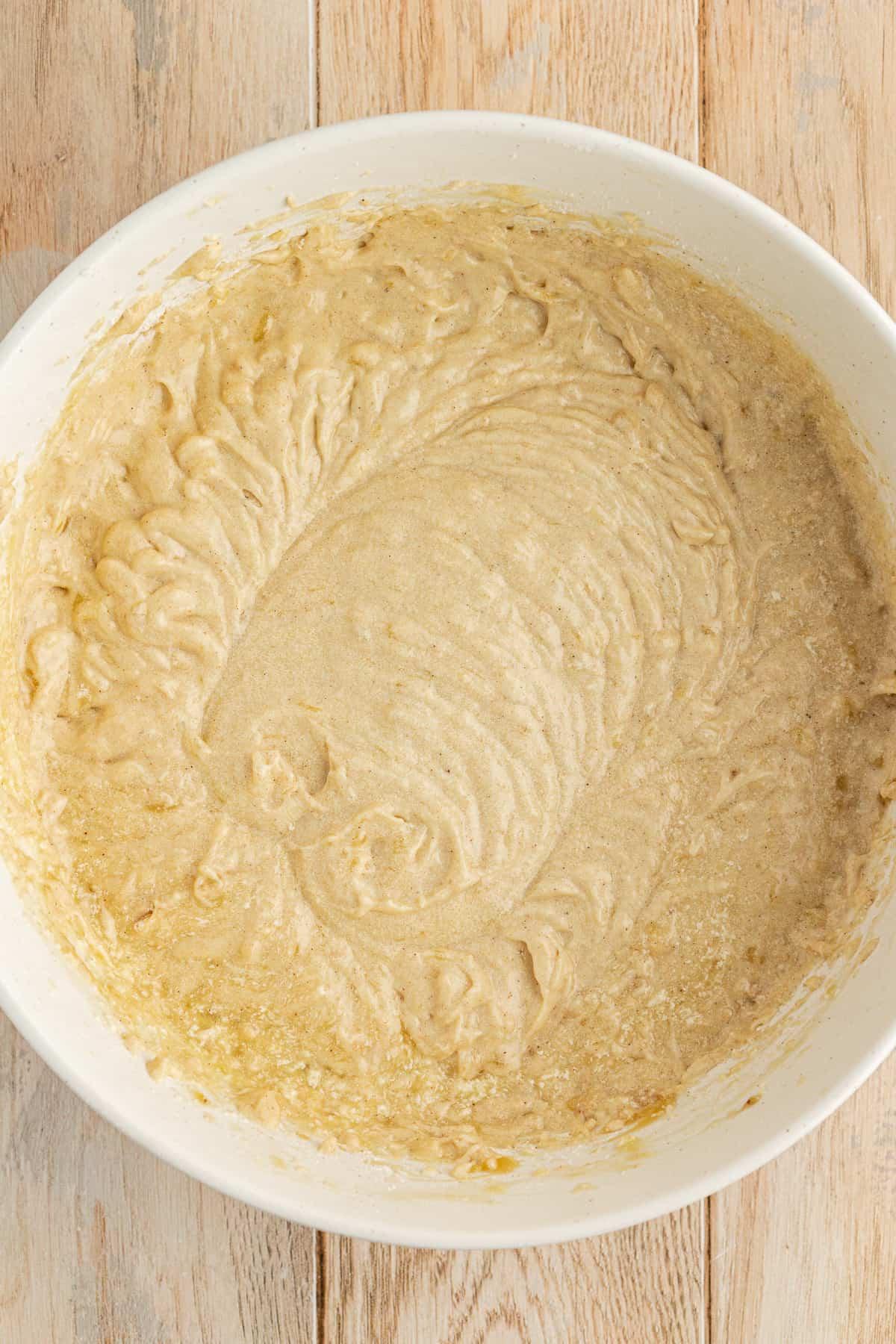 Una ciotola bianca su una superficie di legno piena di impasto di torta di banane