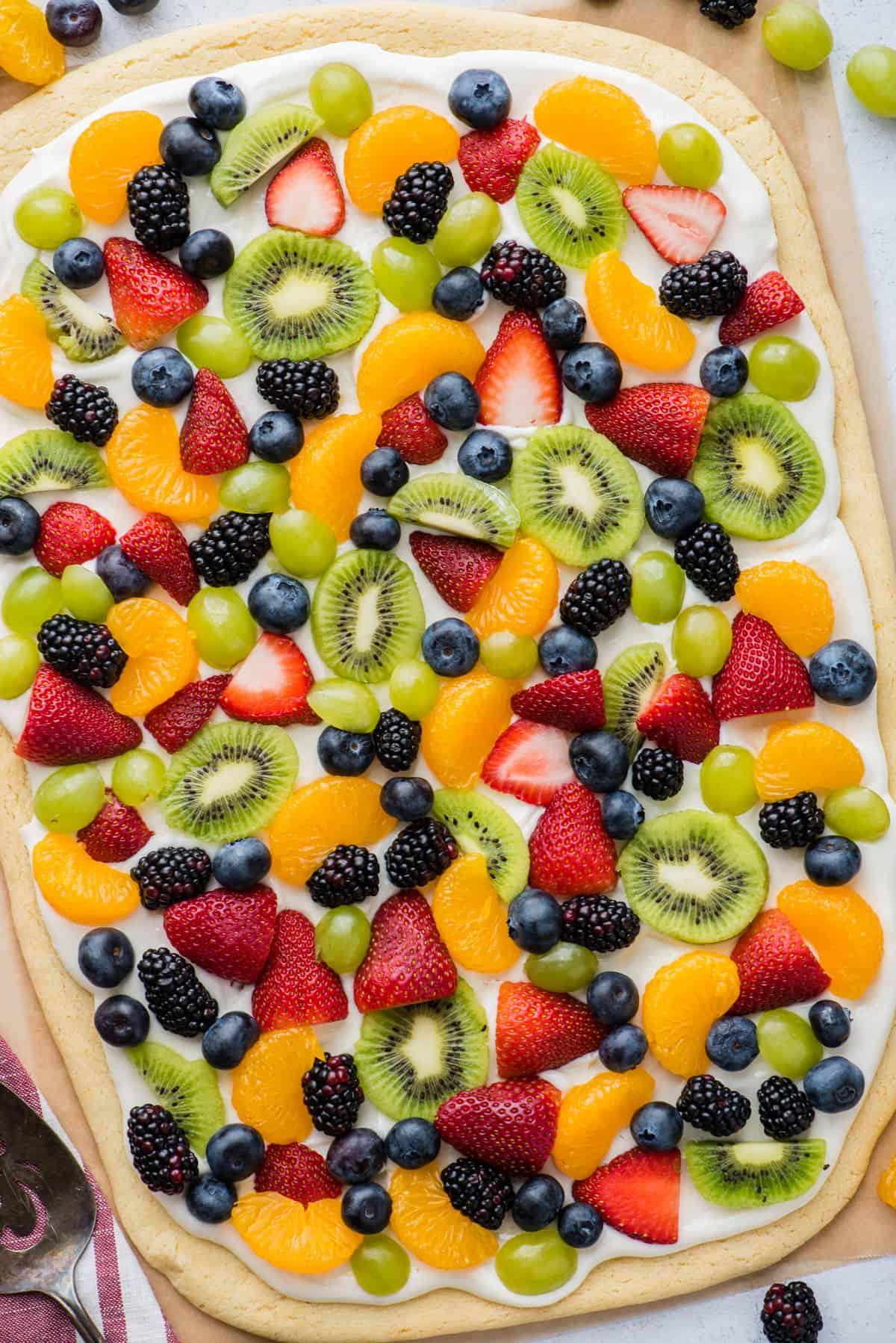La Migliore Ricetta di Pizza alla Frutta 13 Una pizza di frutta intera con fragole, mirtilli, mandarini, kiwi e uva su carta da forno marrone