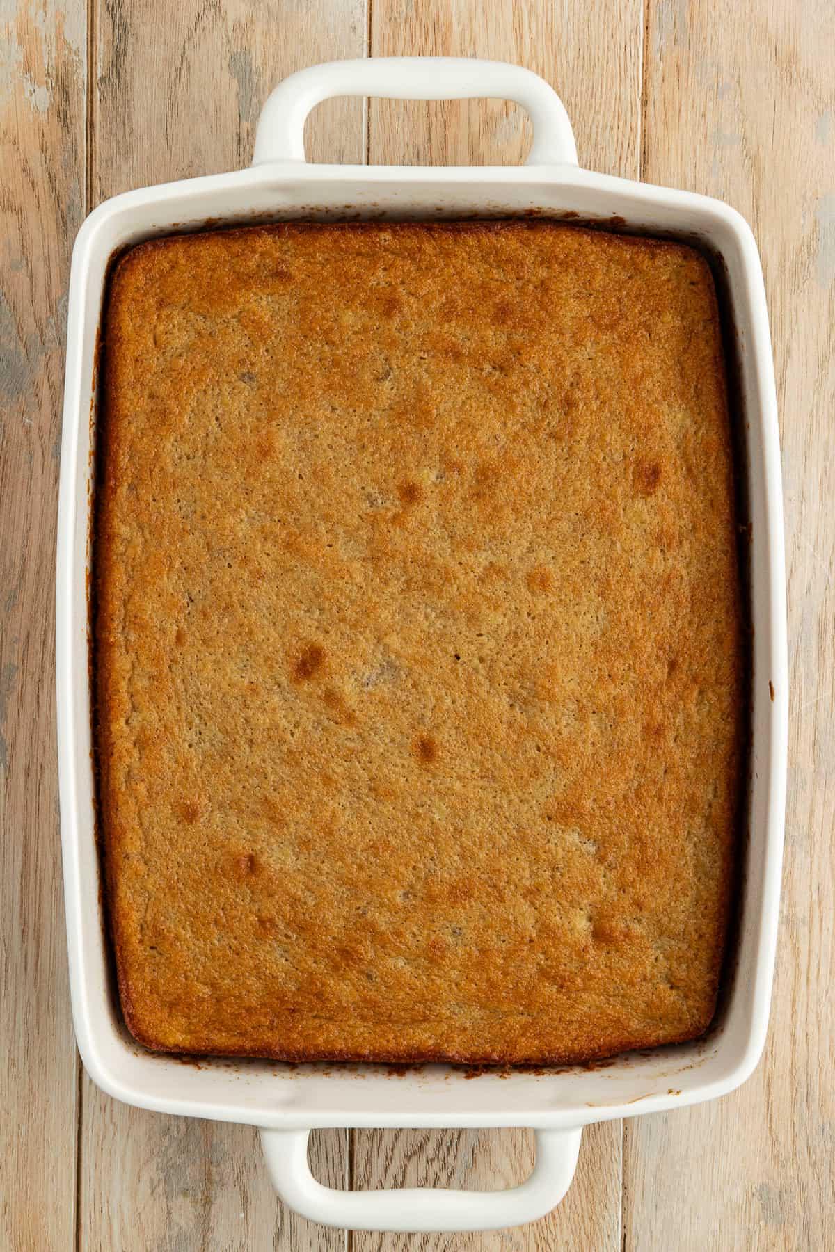 Torta di banane appena sfornata in una teglia bianca da 9x13 su una superficie di legno