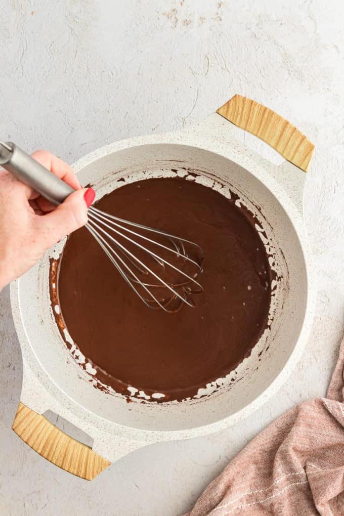 Glassa al cioccolato in una casseruola mescolata con una frusta a filo e un panno da cucina color cuoio a sinistra