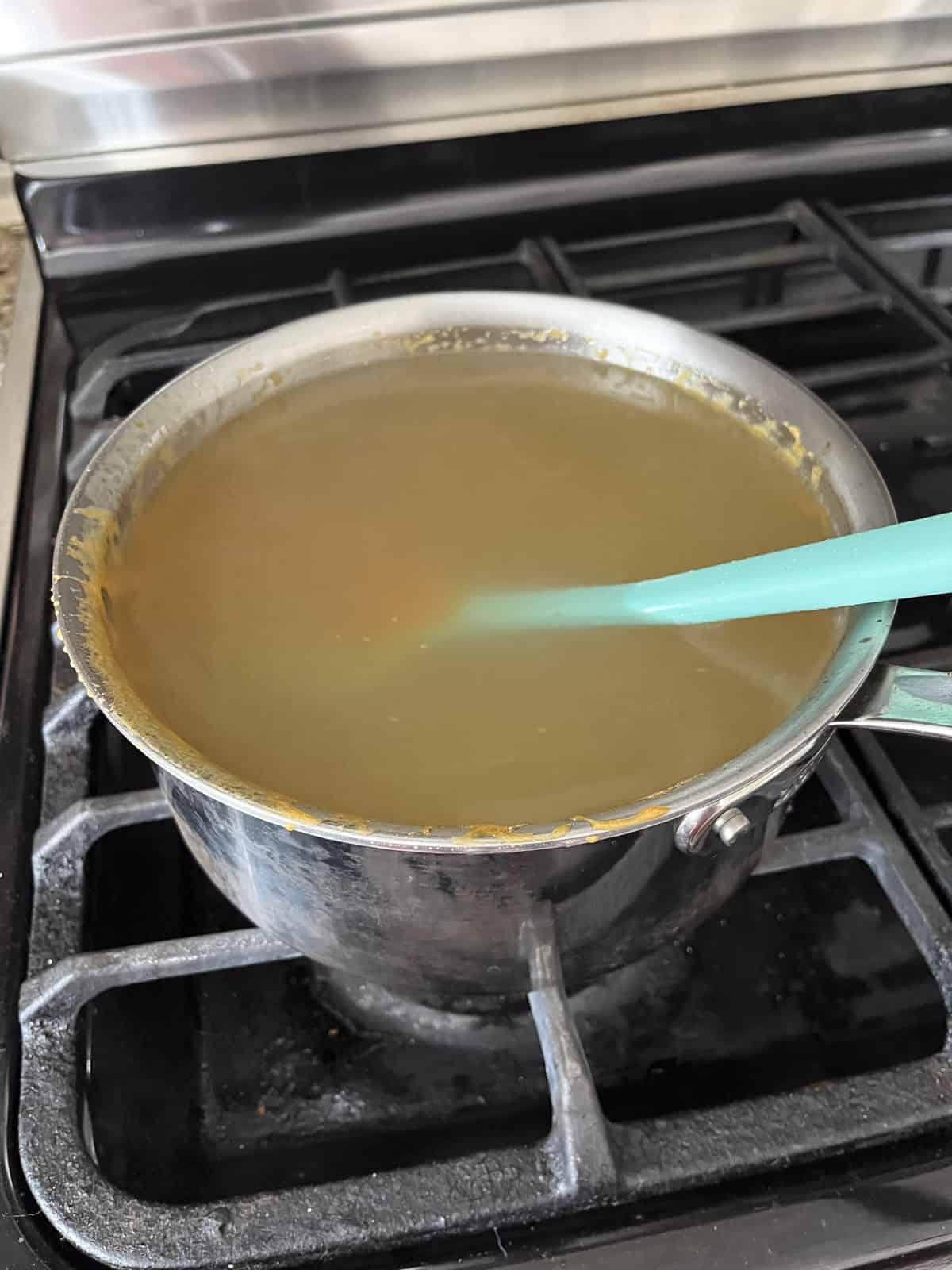 Una pentola sul fornello piena d'acqua e residui di dolci avanzati dalla preparazione del croccante di arachidi con una spatola di gomma all'interno