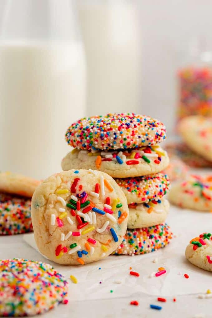Una pila di 5 biscotti Funfetti con preparato per torte con un altro biscotto appoggiato verticalmente sulla pila e altri biscotti Funfetti sparsi intorno