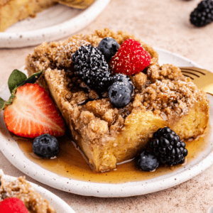 Una fetta di casseruola di French Toast su un piattino con sciroppo d'acero e frutti di bosco freschi
