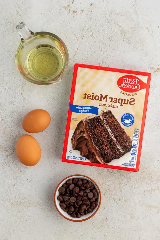 Ingredienti per biscotti doppio cioccolato con preparato per torte, inclusi una scatola di preparato per torte al cioccolato, una ciotola di gocce di cioccolato, due uova e olio vegetale