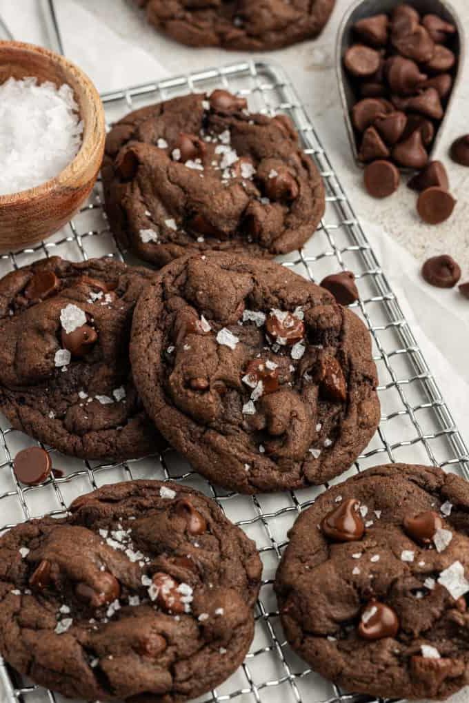 Biscotti doppio cioccolato con preparato per torte su una griglia con gocce di cioccolato sparse intorno e una piccola ciotola di legno di sale
