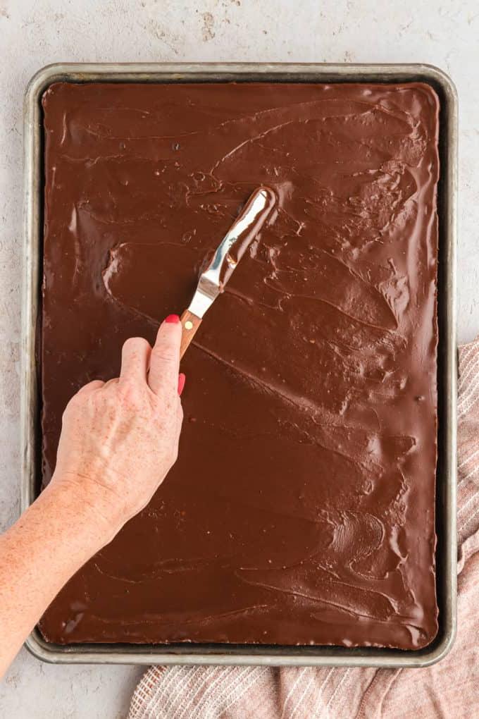 Glassa al cioccolato spalmata su una torta Texana al cioccolato con un coltello da burro 