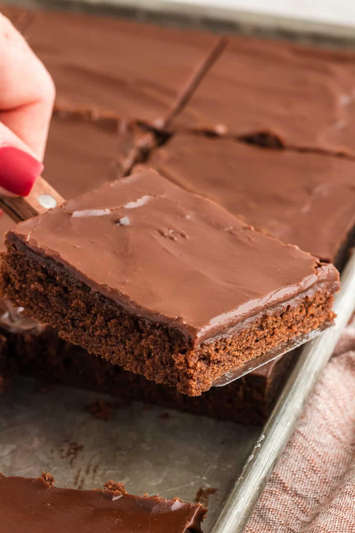 Una fetta di torta Texana sollevata con una spatola da una teglia piena di fette di torta