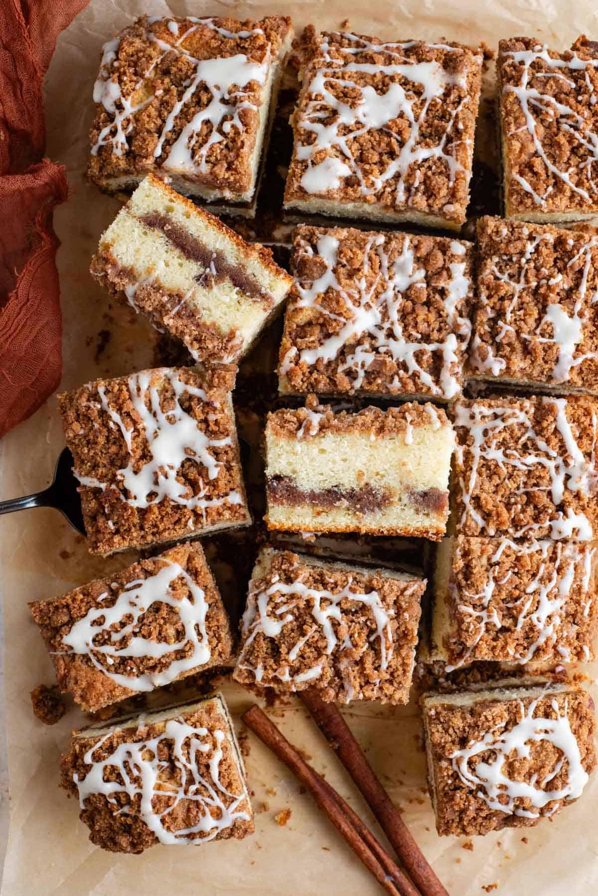 Fette di torta al caffè disposte su carta marrone, alcune di lato, una forchetta, un asciugamano arancione e bastoncini di cannella