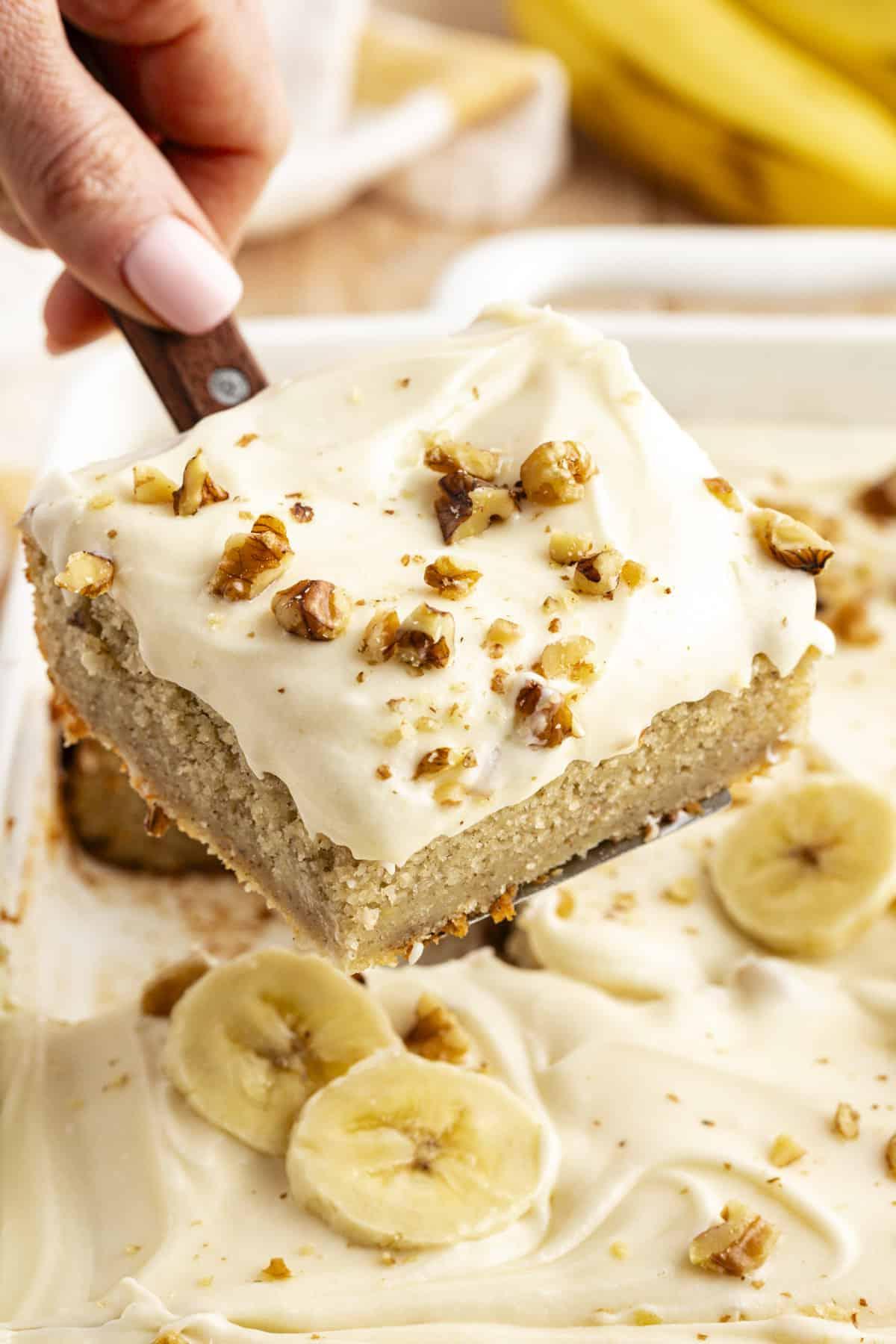 Una fetta di torta di banane con noci tritate cosparse sopra, sollevata dalla teglia con una spatola