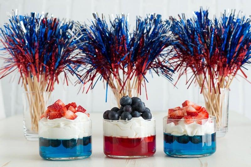 Bicchierini di gelatina blu e rossa con panna montata e fragole e mirtilli tritati
