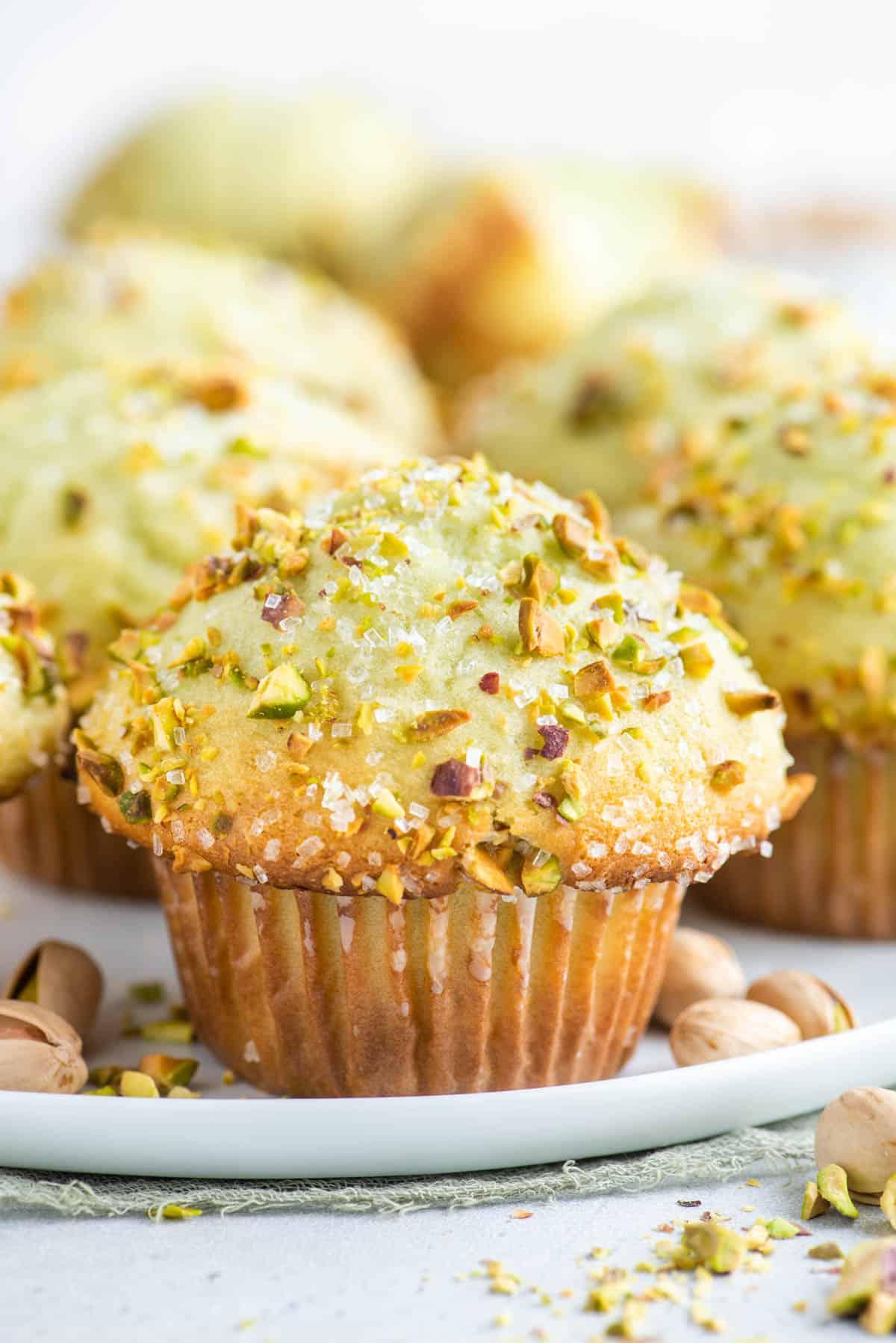Muffin al Pistacchio 3 Pistachio muffins on a white plate with whole pistachios sprinkled around.