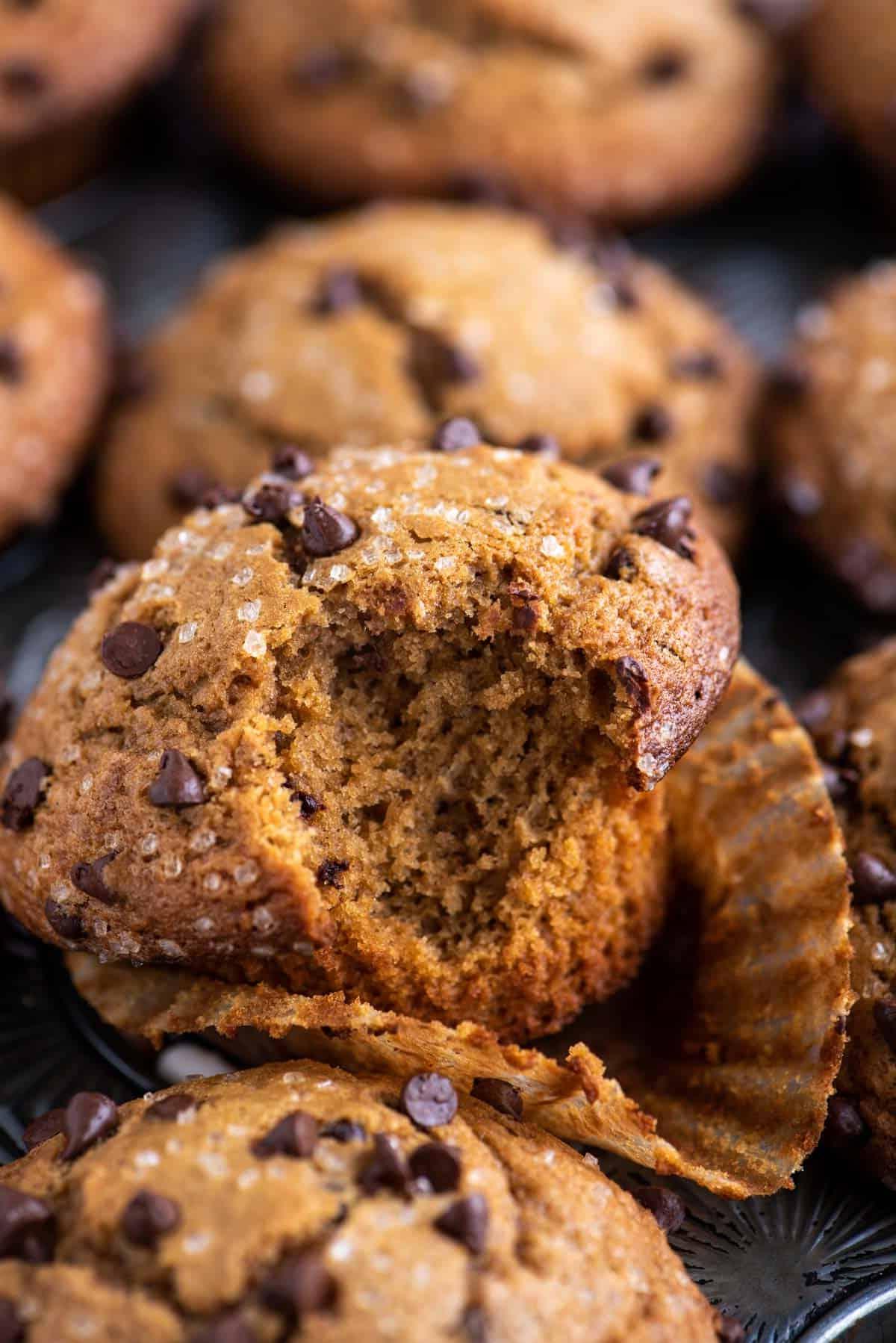 Muffin al Cappuccino e Gocce 3 un muffin al cappuccino con gocce di cioccolato con un morso preso, appoggiato nel suo pirottino su una teglia per muffin piena di altri muffin