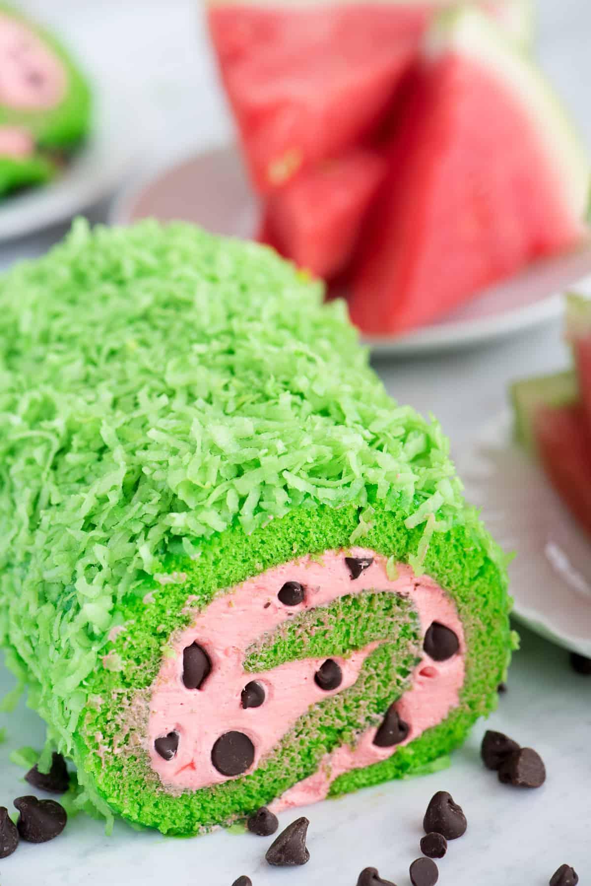 Rotolo all'Anguria 3 Un rotolo di torta dall'aspetto fresco e verde con ripieno rosa e gocce di cioccolato, che richiama l'aspetto di una fetta di anguria.