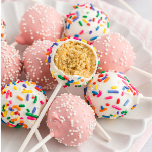 un piatto bianco con una pila di cake pops, alcuni rosa chiaro con codette bianche e alcuni bianchi con codette arcobaleno, con il cake pop in cima a cui manca un morso