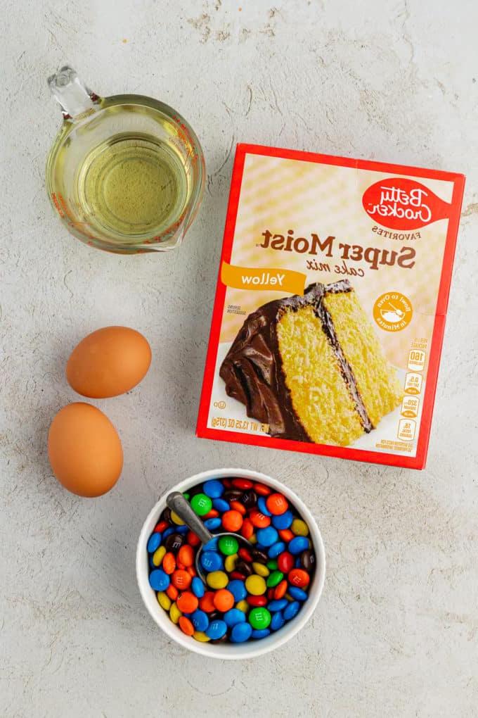 Ingredienti per biscotti M&M, inclusi olio vegetale, due uova grandi e una piccola ciotola bianca di M&M's