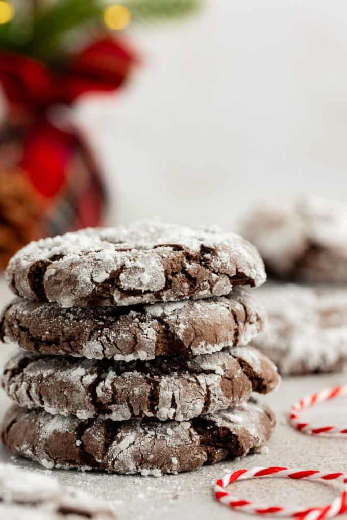 4 biscotti Chocolate Crinkle con preparato per torte impilati con zucchero a velo sparso intorno, uno spago bianco e rosso accanto alla pila e altri biscotti sullo sfondo