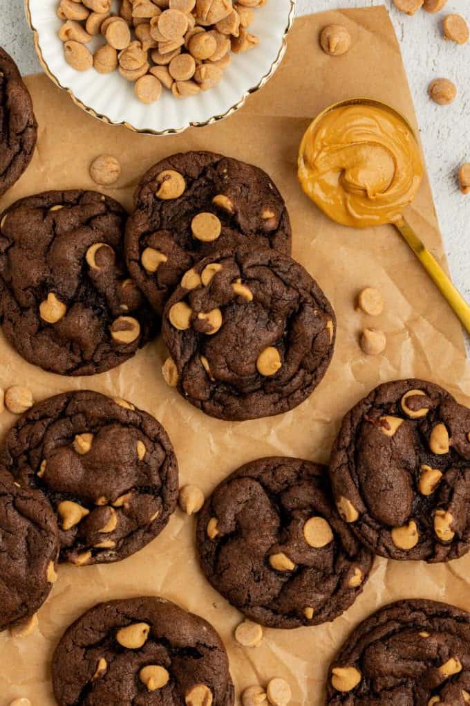Biscotti cioccolato e burro d'arachidi con preparato per torte su carta marrone con un cucchiaio di burro d'arachidi, una ciotola bianca di gocce di burro d'arachidi e altre gocce di burro d'arachidi sparse