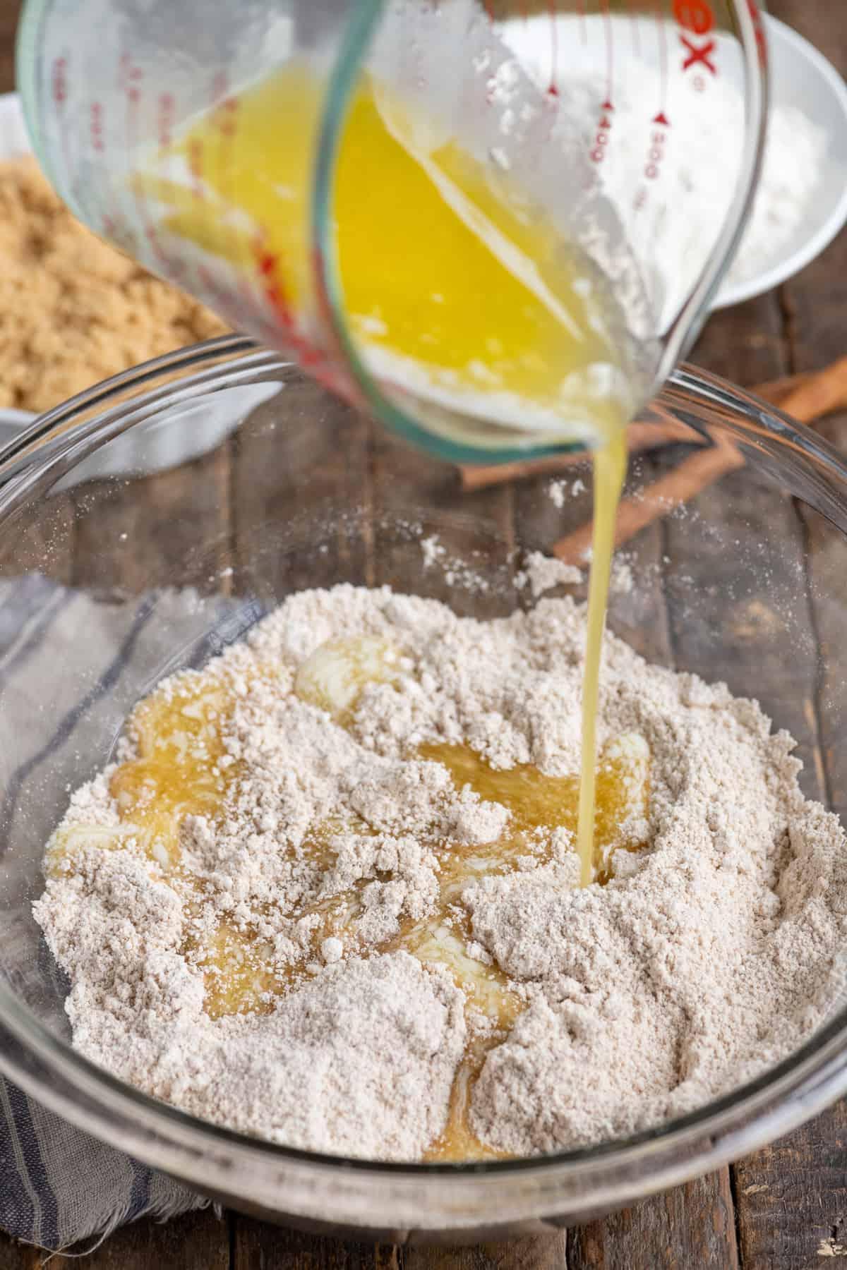 Ricetta della Copertura Sbriciolata 4 burro fuso versato in ciotola di vetro con miscela di copertura sbriciolata su sfondo di legno