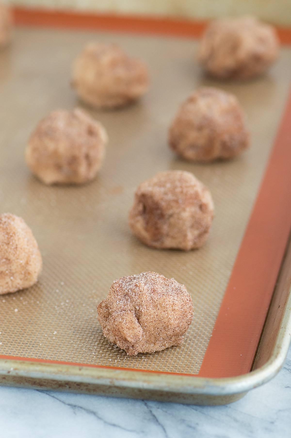 Palline di impasto per snickerdoodle alle mele caramellate allineate su un tappetino di silicone su una teglia metallica