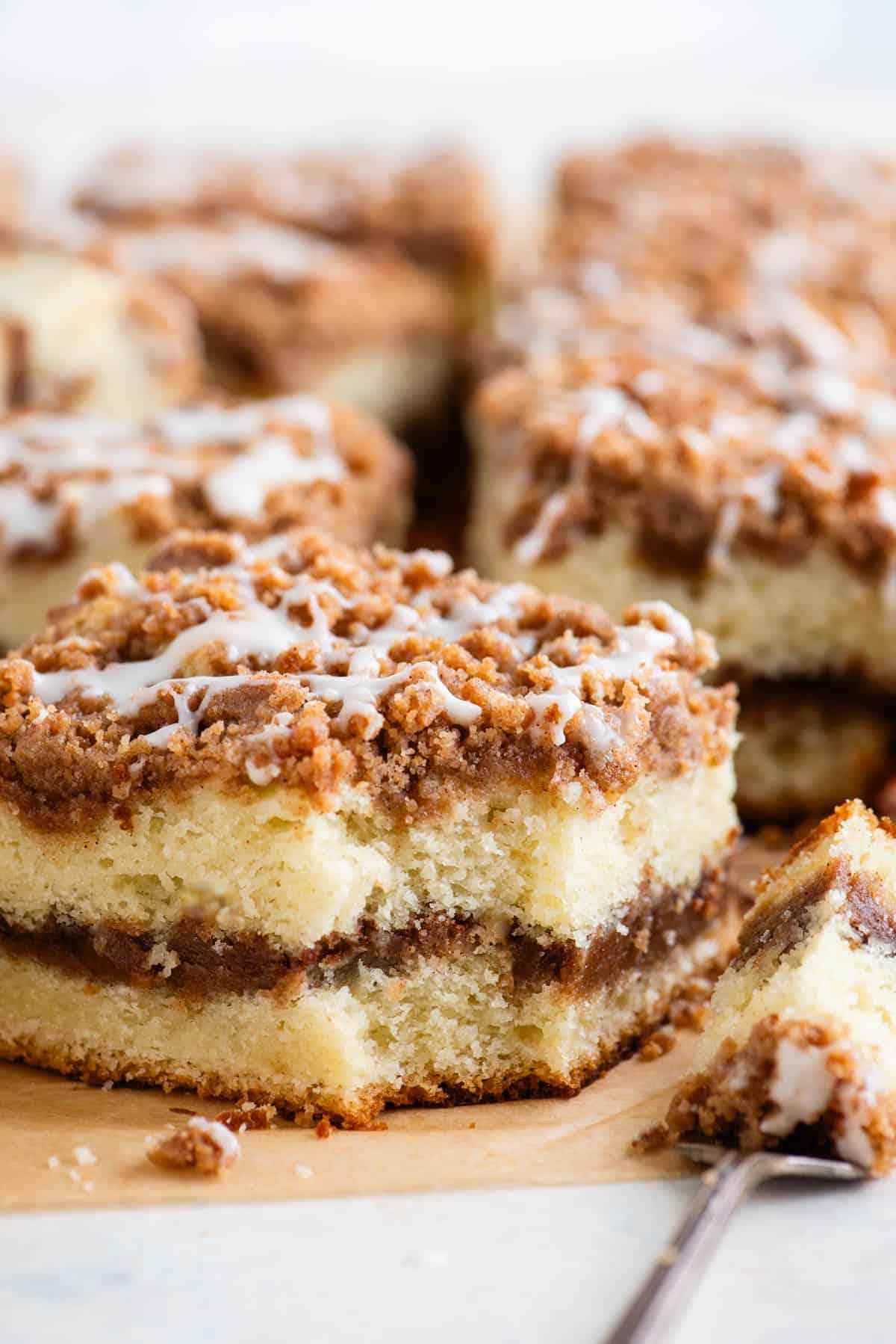 Una fetta di torta al caffè con un morso preso, poggiata su una forchetta accanto alla fetta e altre fette di torta sullo sfondo