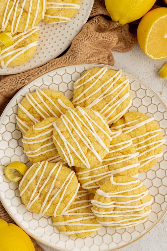 Biscotti al limone con preparato per torte su un piatto a nido d'ape circondato da panno beige, limoni e un altro piatto di biscotti sullo sfondo
