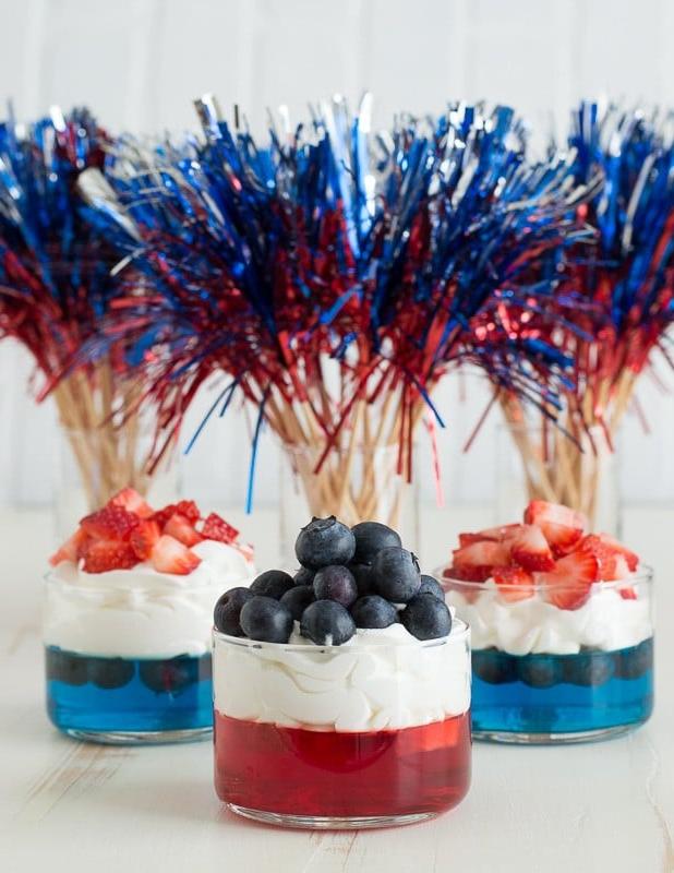 Bicchierini di gelatina blu e rossa con panna montata e fragole e mirtilli tritati