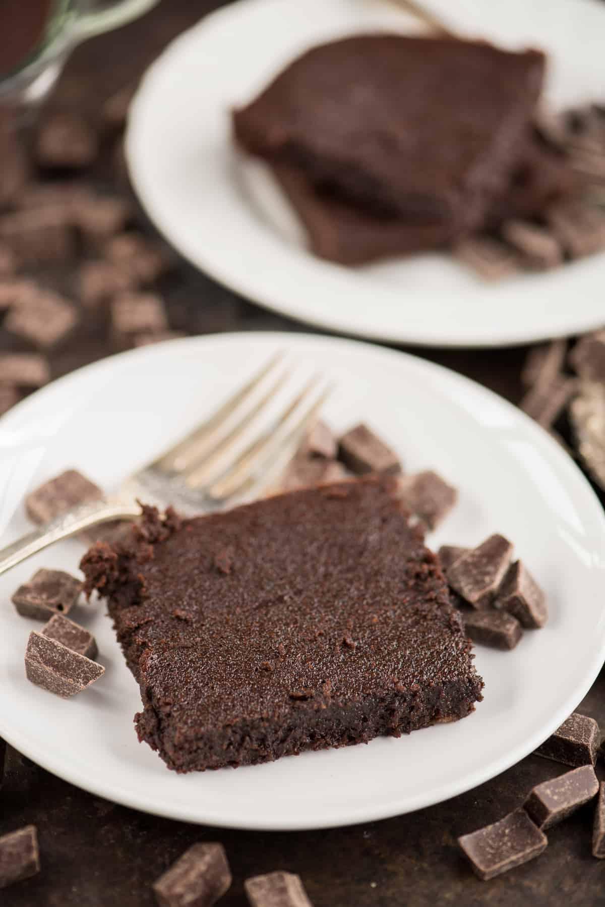 Un brownie fondente salutare con piccoli pezzi di cioccolato e una forchetta d'argento su un piatto bianco.